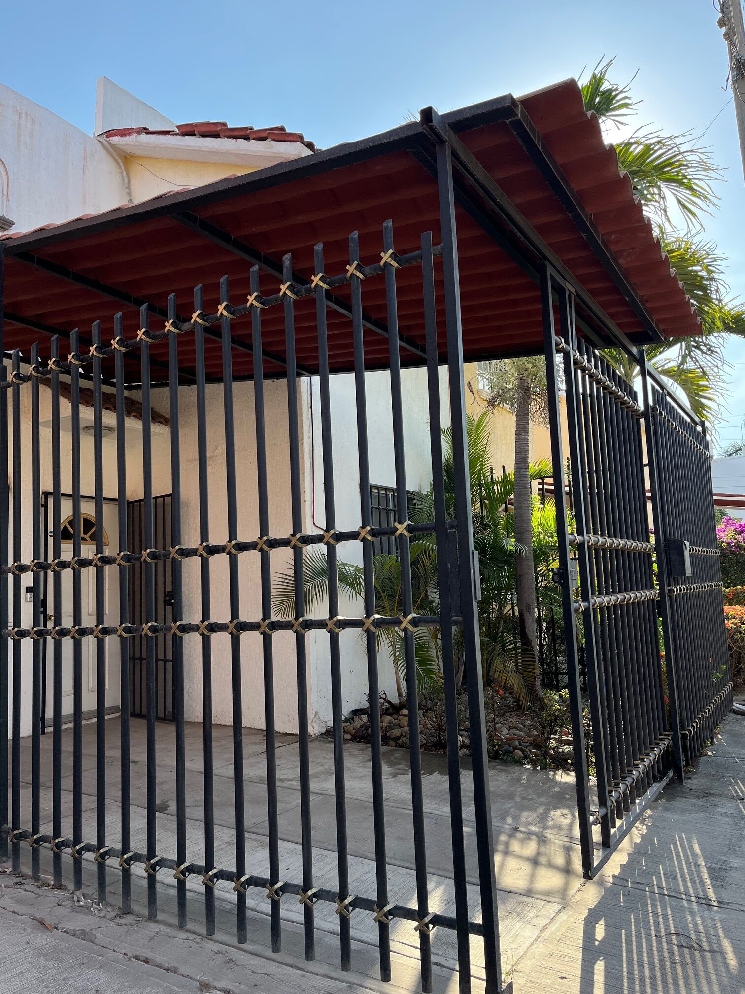 A gated area with a metal fence, a covered walkway, and a building with a white facade.