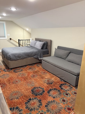 A bedroom with a bed, a sofa, a patterned rug, and a staircase.
