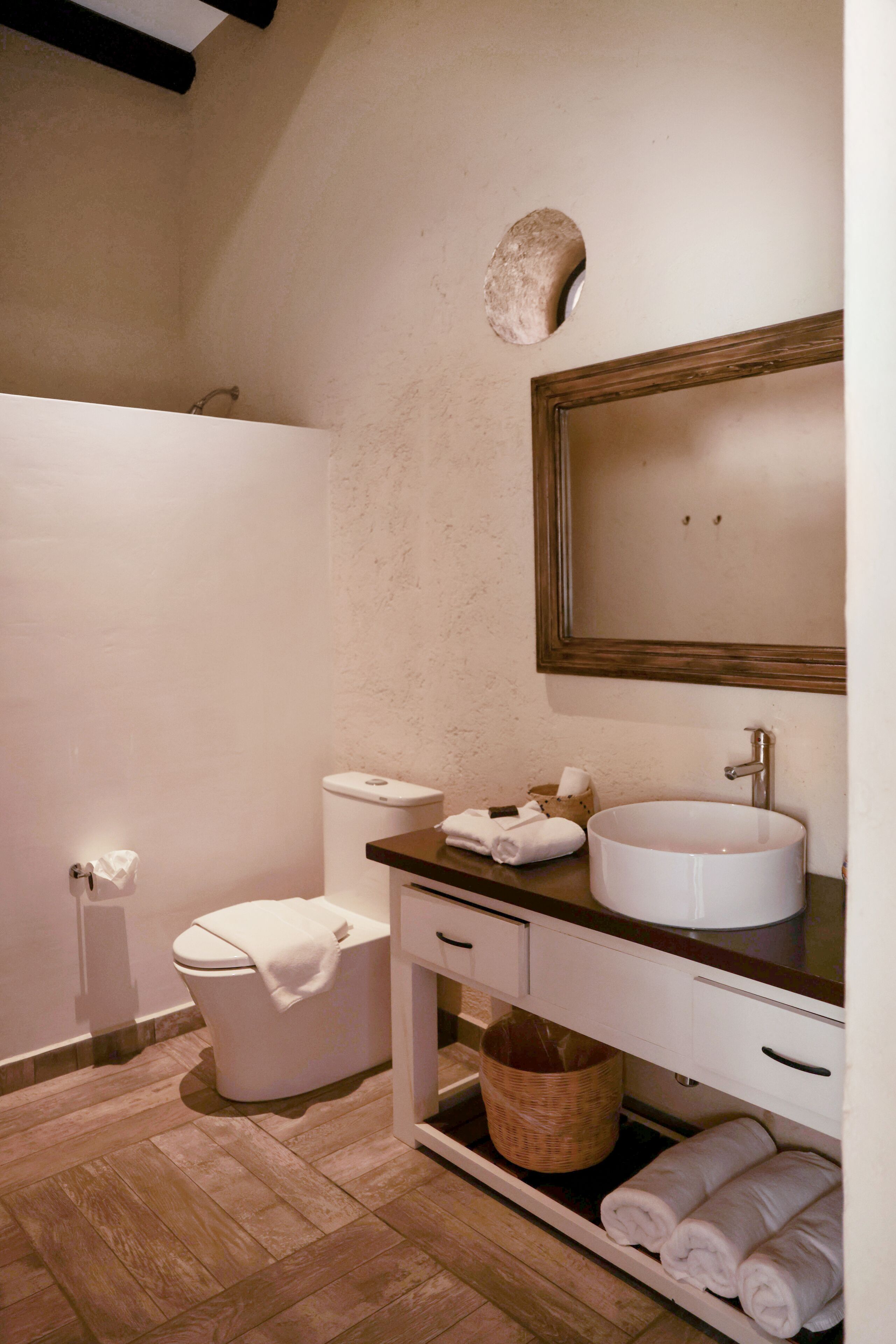 A bathroom with a toilet, sink, and mirror. There are towels and a basket on the counter.