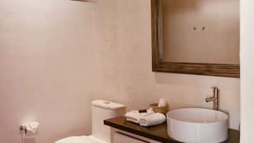 A bathroom with a toilet, sink, and mirror. There are towels and a basket on the counter.