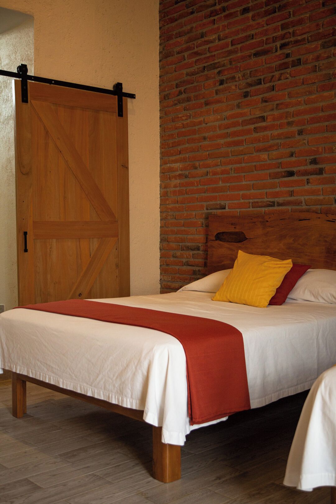 A bedroom with a wooden bed, a red and white bedspread, and a brick wall.