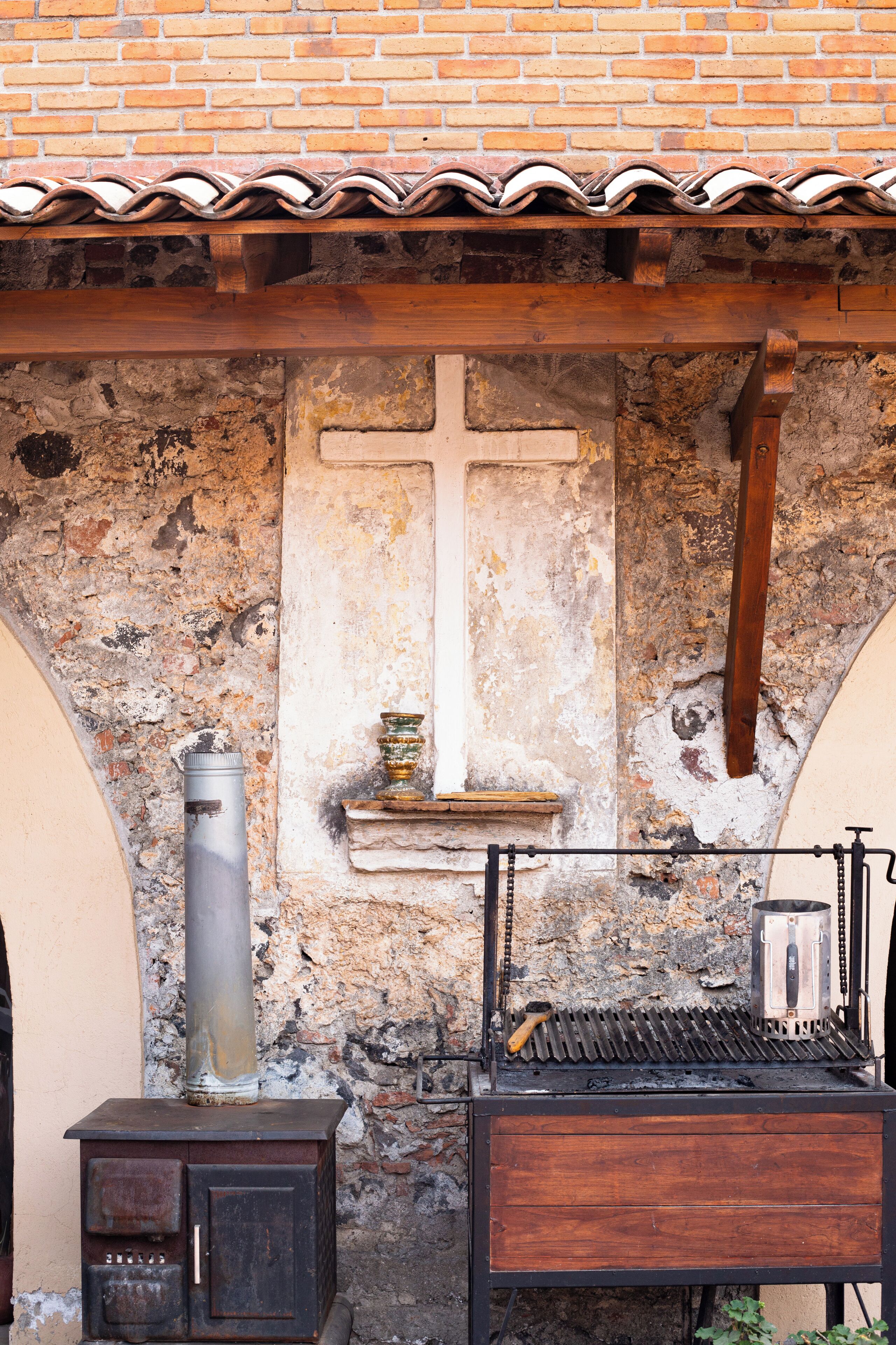 A rustic stone wall with a cross, a metal stove, and a wooden cabinet.