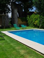 Una piscina con dos sillones reclinables verdes, un muro de piedra y una valla de madera.