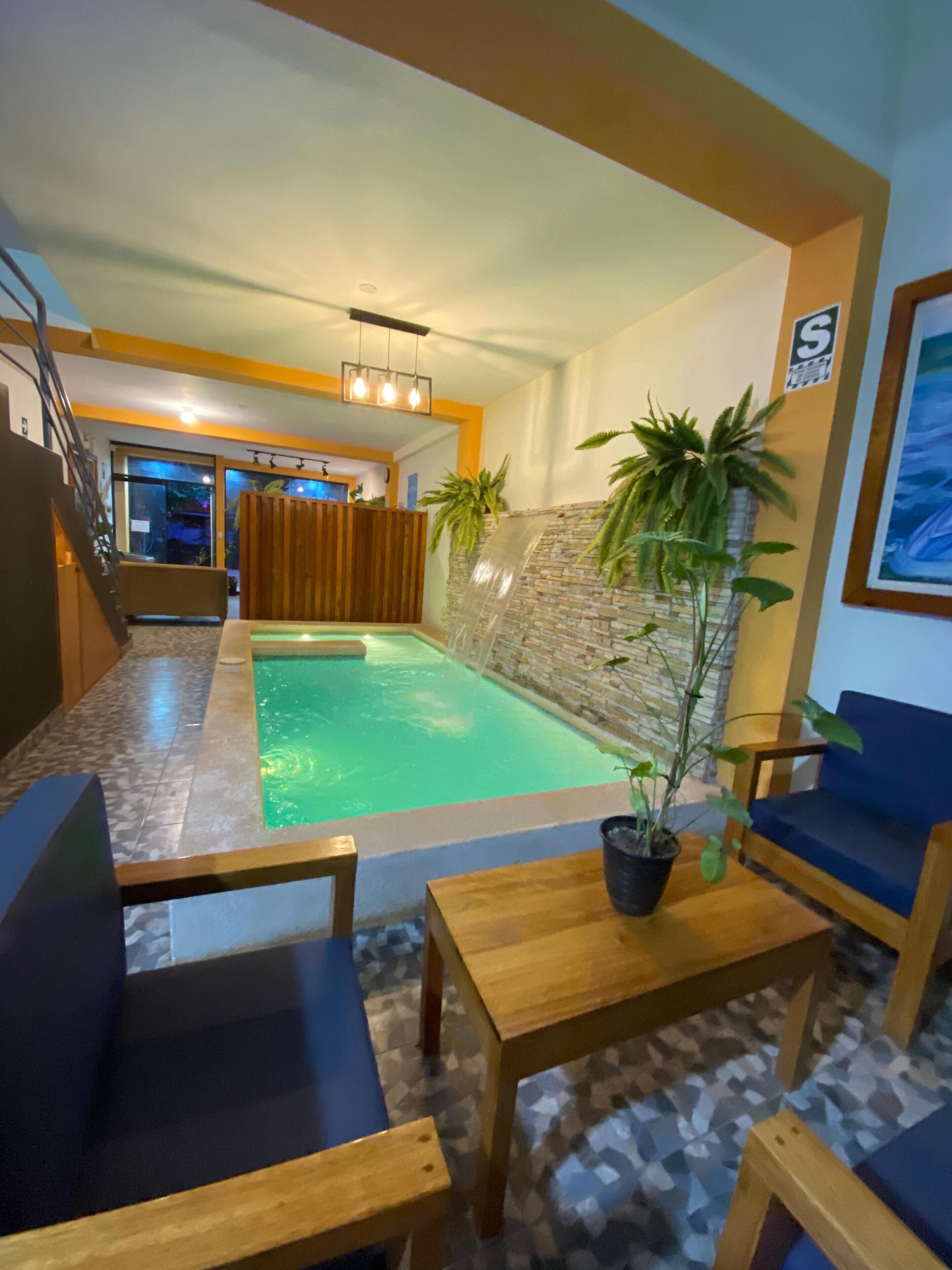 A pool area with a waterfall feature, wooden furniture, and a potted plant.