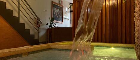 A hot tub with a waterfall feature, a staircase, and a wooden wall with a plant.