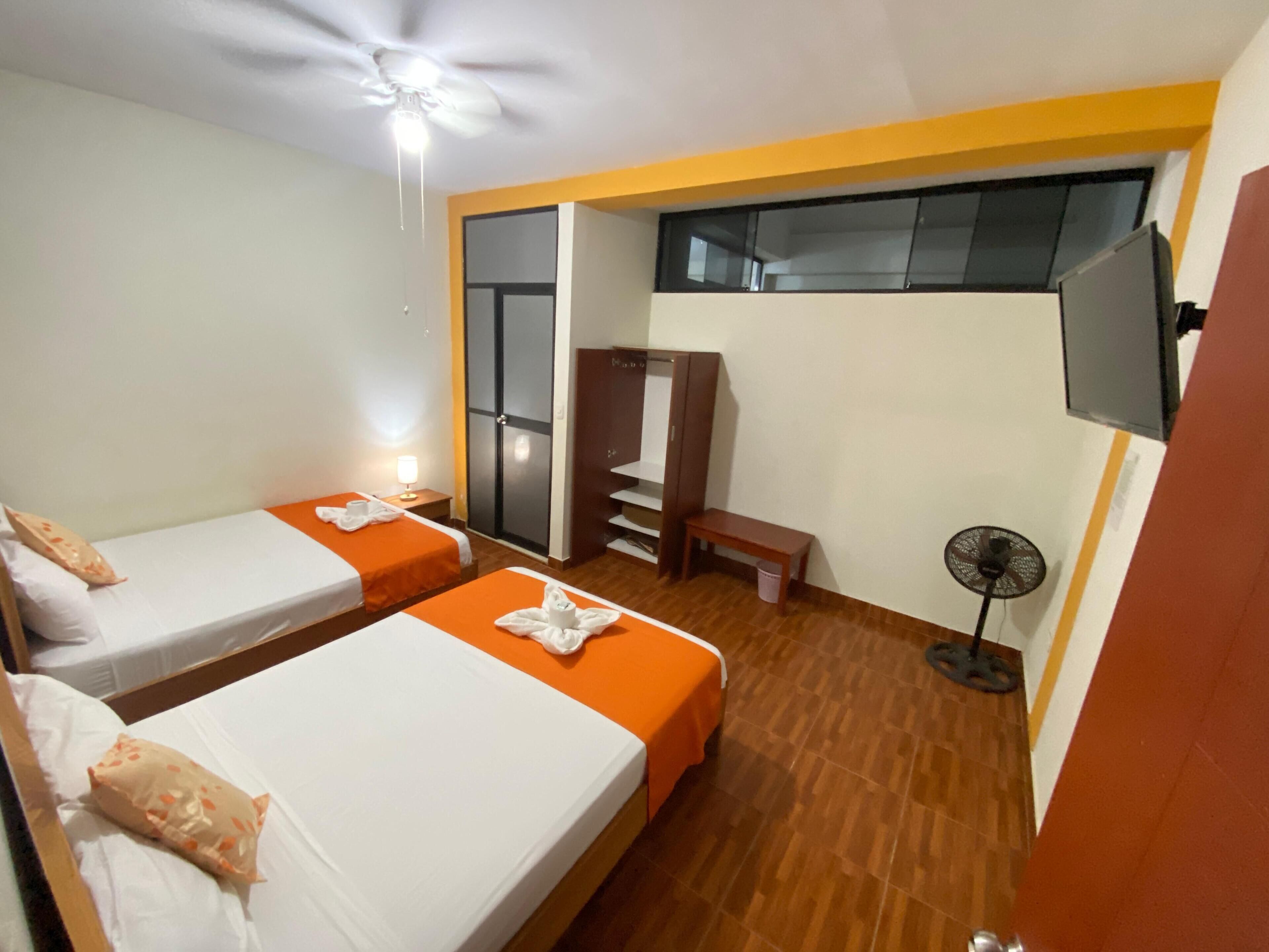 A hotel room with two beds, a wardrobe, a TV, and a ceiling fan.