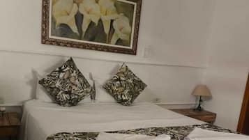 A neatly made bed with floral-patterned bedding, two pillows with a similar design, a framed artwork above the bed, and a bedside lamp on a wooden nightstand.