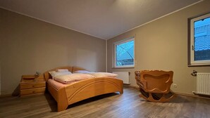 A bedroom with a wooden bed, a nightstand, a dresser, a chair, and a window with a view of trees. - Villa in the middle of Haselünnne (Haselünne)