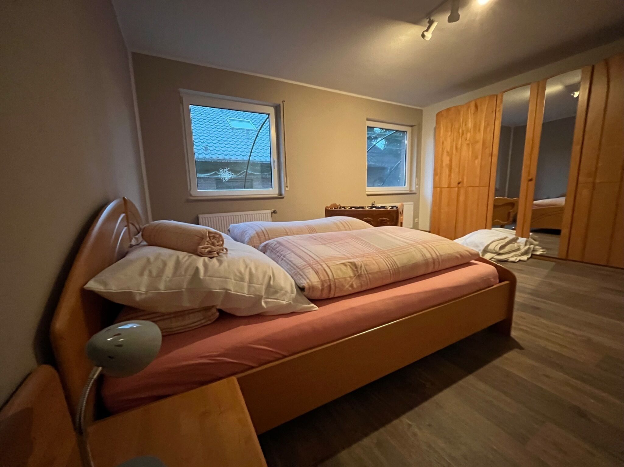 Ein Schlafzimmer mit Bett, Nachttisch, Lampe, Fenstern und einem Kleiderschrank.