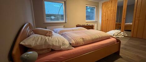 Ein Schlafzimmer mit Bett, Nachttisch, Lampe, Fenstern und einem Kleiderschrank.