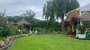A well-maintained garden with a gazebo, a large tree, and a variety of flowering plants. - Villa in the middle of Haselünnne (Haselünne)