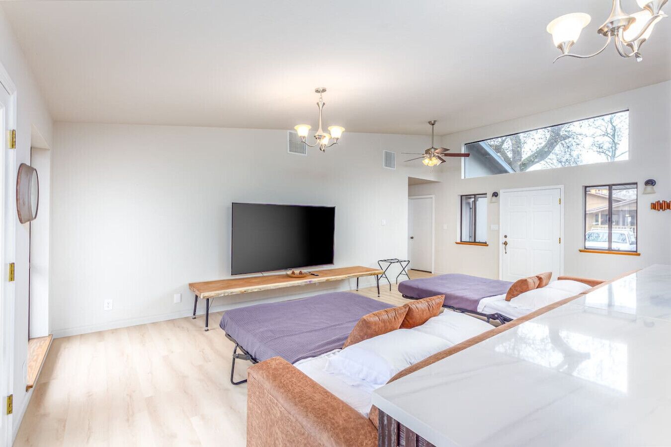 Habitación de hotel moderna con dos camas, un televisor de pantalla plana, un banco de madera y un ventilador de techo.