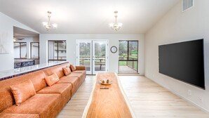 Ett rymligt vardagsrum med en stor soffa, ett soffbord i trä, en platt-TV och en skjutdörr i glas som leder ut till en uteplats.