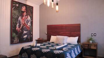 Un dormitorio con una cama grande, cabecera de madera, un cuadro en la pared y una mesita de noche con una planta.