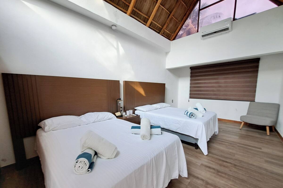 Quarto de hotel com duas camas, teto de madeira e janela com persianas.