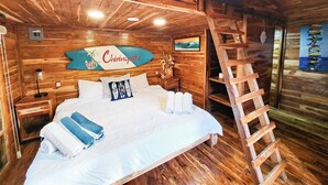 A wooden cabin-style room with a bed, a ladder, a surfboard sign, and a framed picture on the wall. - Hotel Chiringuito de Palo (Aticama)
