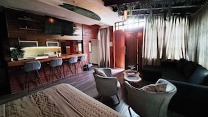 A modern hotel room with a kitchen area, a dining table with bar stools, a sofa, and a large bed. - Hotel Chiringuito de Palo (Aticama)