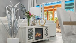 A modern living room with a white sofa, a decorative console table with a fireplace, and a view of the outdoors. - 3113 Amazing Poolside Villa ~ Super DEAL ~ Book Sept 7th ~ Lagoon Pool ~ Hot Tub (Destin)