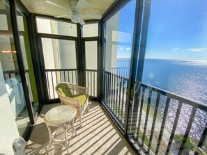 A balcony with a view of the ocean, a ceiling fan, and two wicker chairs.