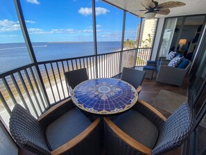 A balcony with a view of the ocean, wicker furniture, and a tiled table.