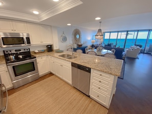 A modern kitchen with built-in appliances, a large island with a sink, and a view of the ocean through large windows.