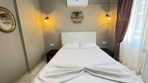 Une chambre d’hôtel comprenant un lit, deux tables de chevet, un climatiseur fixé au mur et deux appliques murales.