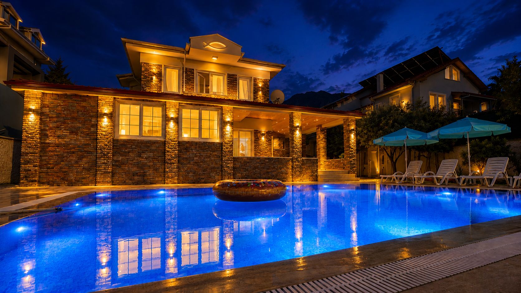 A swimming pool with a stone wall and a house with multiple windows and a satellite dish.
