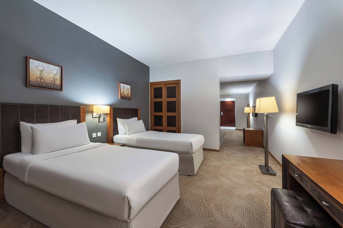 Una habitación de hotel con dos camas, un televisor, un escritorio y una puerta que da a otra habitación.
