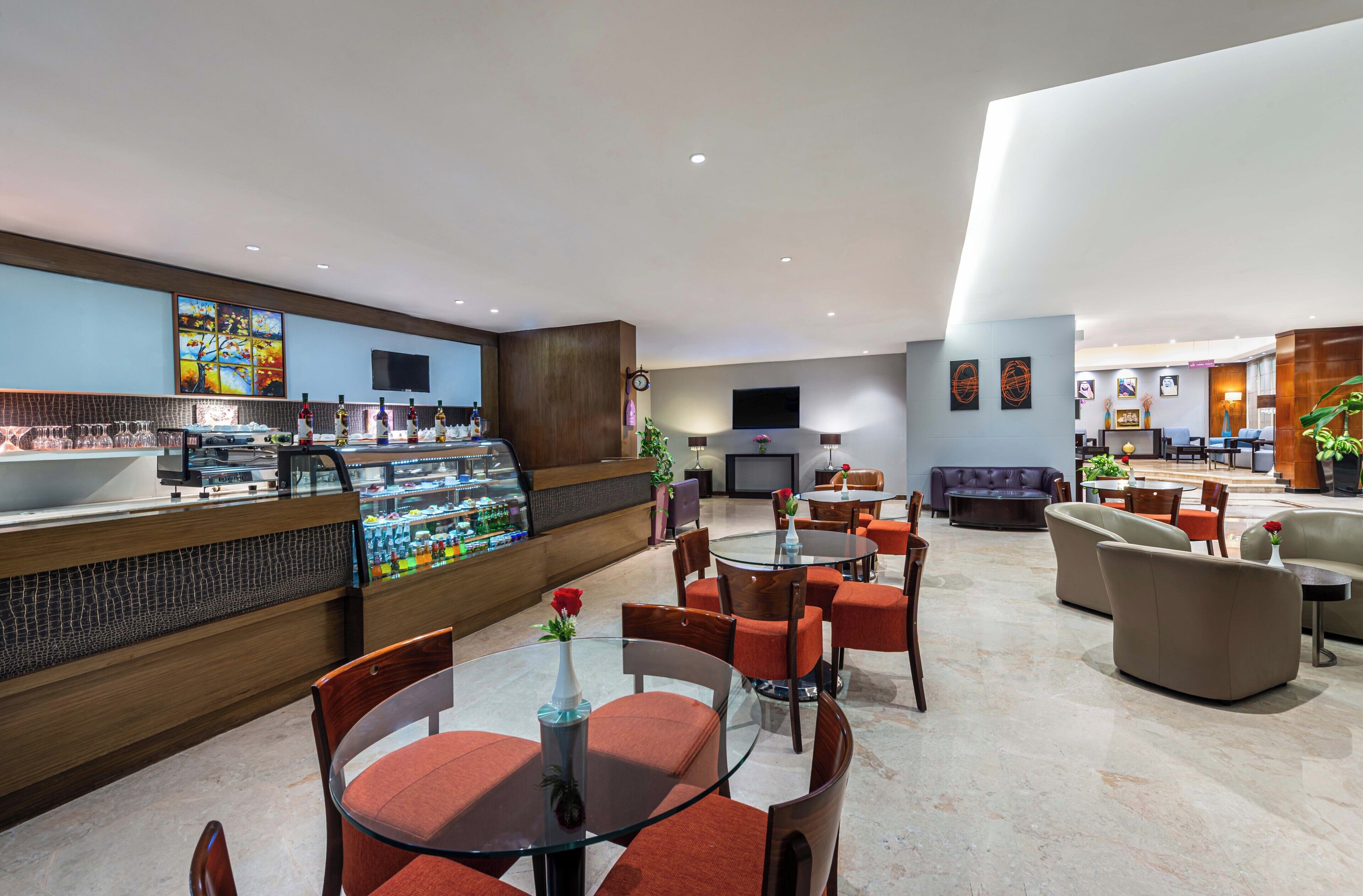 Un moderno vestíbulo de hotel con una zona de bar, disposición de asientos y un televisor en la pared.