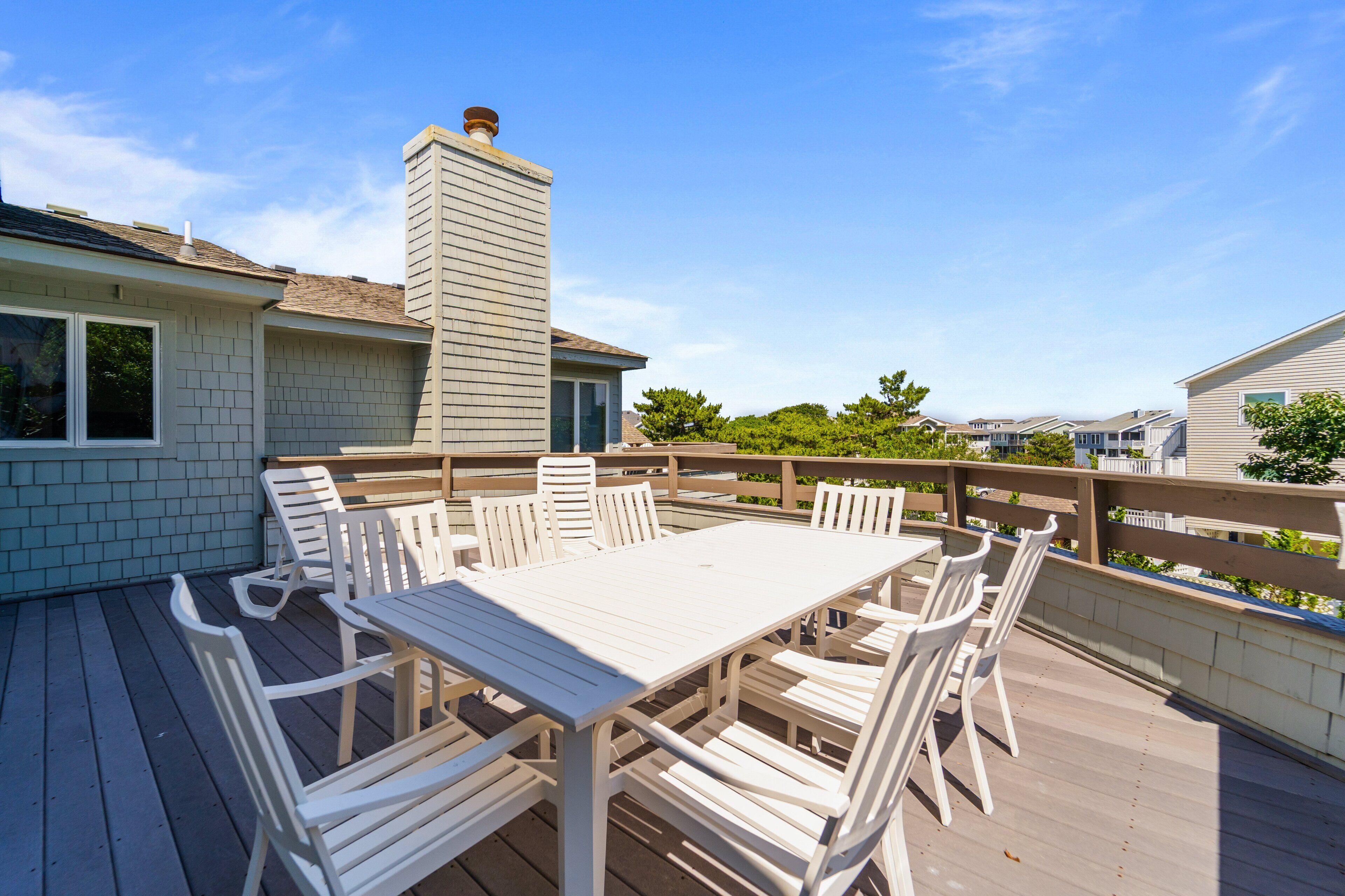 Une terrasse avec une table et des chaises blanches, entourée d’une autre terrasse en bois et d’une rambarde.