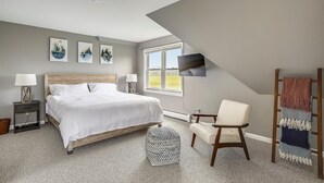 Un dormitorio con cama, mesitas de noche, una silla, televisión y obras de arte en la pared.