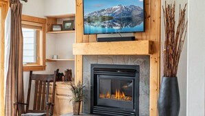 Una sala de estar con chimenea, un televisor montado encima y una ventana con cortinas.