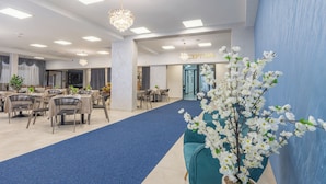 A hotel reception area with a blue carpet, tables, chairs, a chandelier, and a reception desk. - Hotel Mondo  (Budva)
