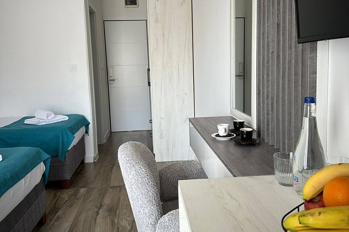 A modern hotel room with two single beds, a small desk with a chair, a television, and a fruit basket.