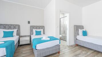 Ein Hotelzimmer mit drei Betten, einem Badezimmer mit Glastür und Holzboden.