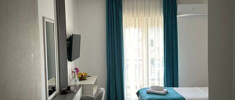 Hotellihuone, jossa on työpöytä, tuoli, kaksi sänkyä ja suuri ikkuna, jossa on verhot.