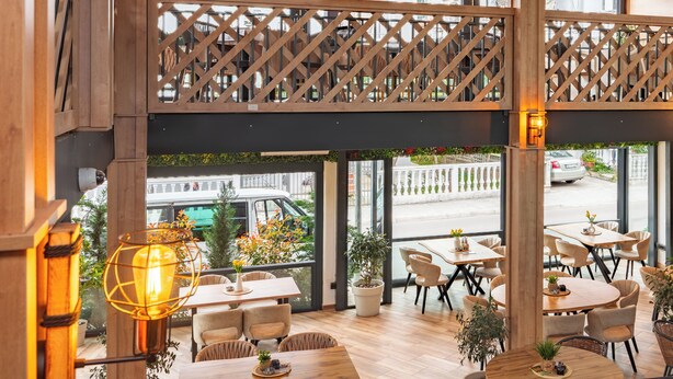 A restaurant with outdoor seating, wooden lattice railings, and large windows offering a view of the street. - Hotel Mondo  (Budva)