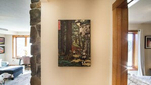 A room with a stone wall, a bed, a desk, and a painting of a forest scene.