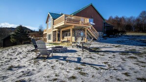 A two-story wooden house with a stone foundation, a covered porch, and a stone fireplace.
