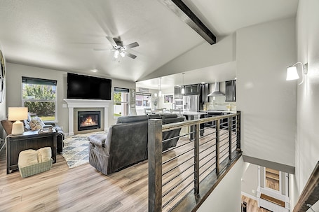 A spacious living room with a fireplace, a ceiling fan, and a kitchen area visible through an open door.