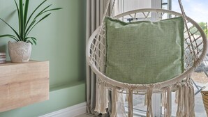 A wicker chair with a green cushion, a potted plant, and a wooden shelf against a green wall. - The Sands BG3 - Two Bedroom Apartment, Sleeps 4 (Cape Town)