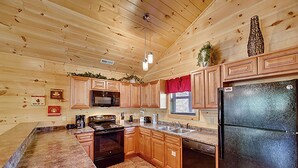 A kitchen with wooden cabinets, a black refrigerator, a microwave, and a stove. - Mountain and River Views: hot tub ~ pool table~ movie theater ~ fire pit (Pigeon Forge)