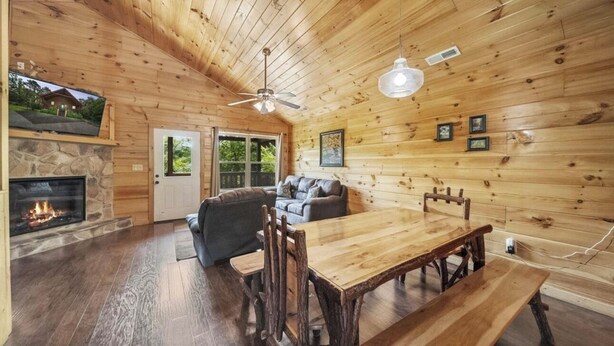 A cozy cabin interior with a stone fireplace, wooden dining table, and a ceiling fan. - Mountain and River Views: hot tub ~ pool table~ movie theater ~ fire pit (Pigeon Forge)