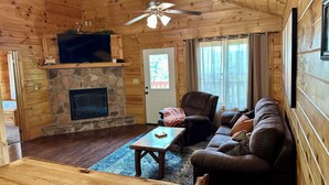 A cozy cabin interior with a stone fireplace, wooden walls, a ceiling fan, and a comfortable seating area. - Mountain and River Views: hot tub ~ pool table~ movie theater ~ fire pit (Pigeon Forge)