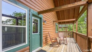 A wooden cabin with a porch, a rocking chair, and a door with a window. - Mountain and River Views: hot tub ~ pool table~ movie theater ~ fire pit (Pigeon Forge)