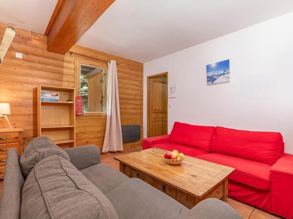 A cozy living room with a red sofa, a grey sofa, a wooden coffee table with fruit, and wooden walls.