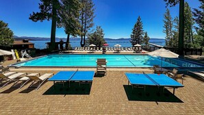 Una piscina con sillones de descanso y sombrillas, rodeada de árboles altos y vistas al mar.