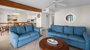 Ein Wohnzimmer mit zwei blauen Sofas, einem Holztisch, einem Deckenventilator und einem runden Spiegel an der Wand.