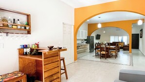 A kitchen with a wooden bar, a dining area with a table and chairs, and an archway leading to another room.
