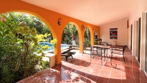 A covered outdoor area with a pool, seating, and plants.